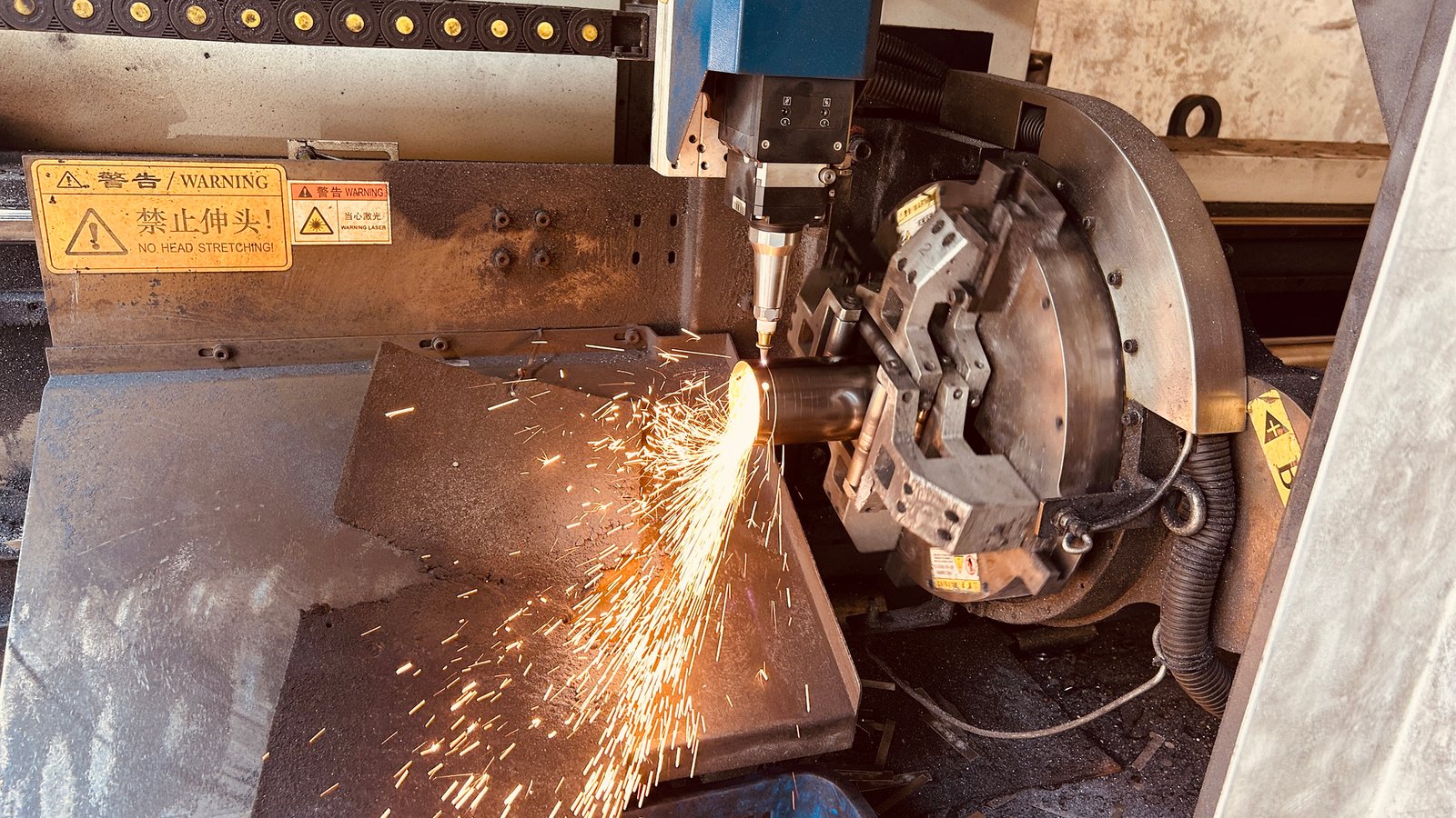 Laser cutting equipment processing a metal tube for mirror hardware as sparks fly